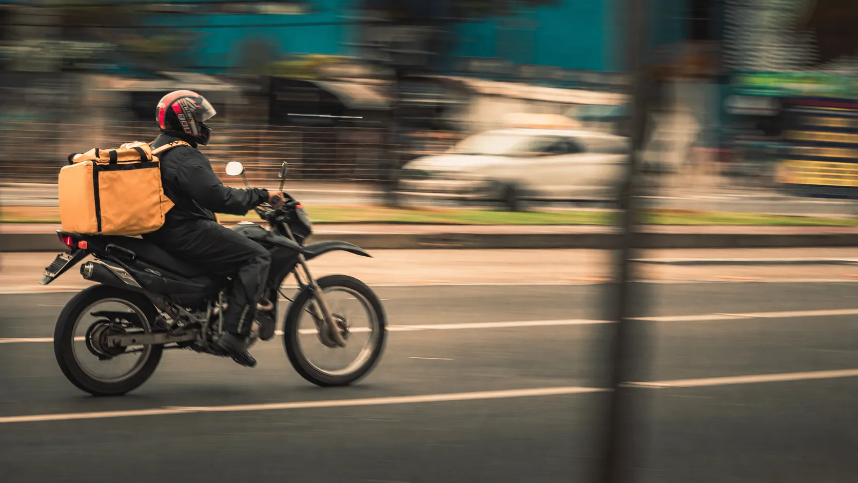 Cadete en moto circulando por la ciudad con el baúl de reparto